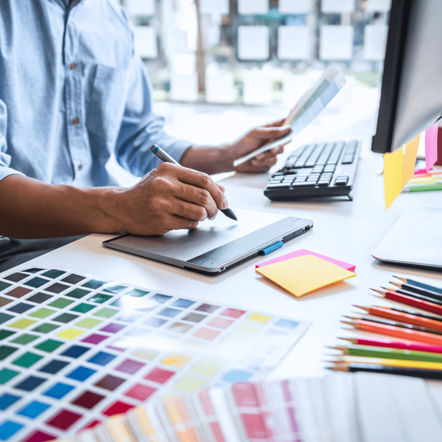 A person using a graphics tablet, surrounded by design tools representing creativity in graphic design.