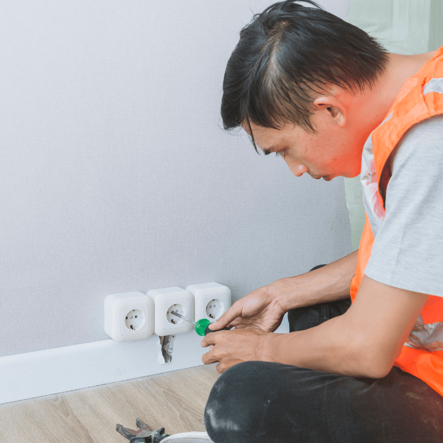 A person in an orange safety vest working as a handyman on electrical outlets with a screwdriver.