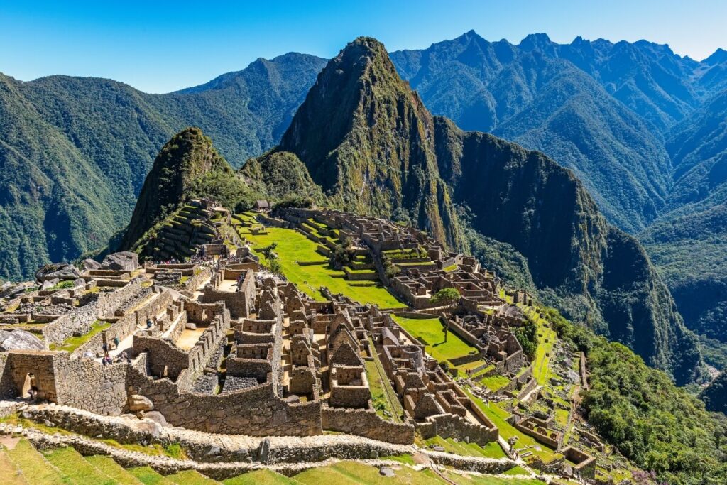 A panoramic view of Machu Picchu, the ancient Inca city nestled in the Andes Mountains, showcasing its terraced slopes, stone structures, and lush greenery under a clear blue sky.