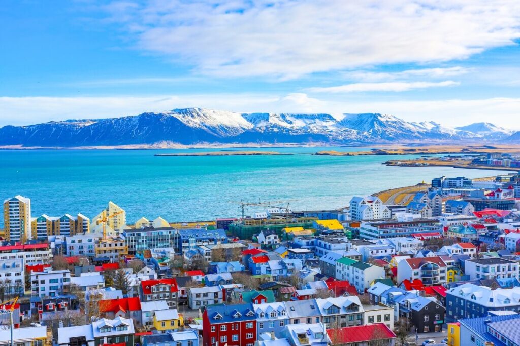 Colorful buildings in Reykjavik, Iceland, with rolling hills and Faxaflói Bay in the background under a clear blue sky.