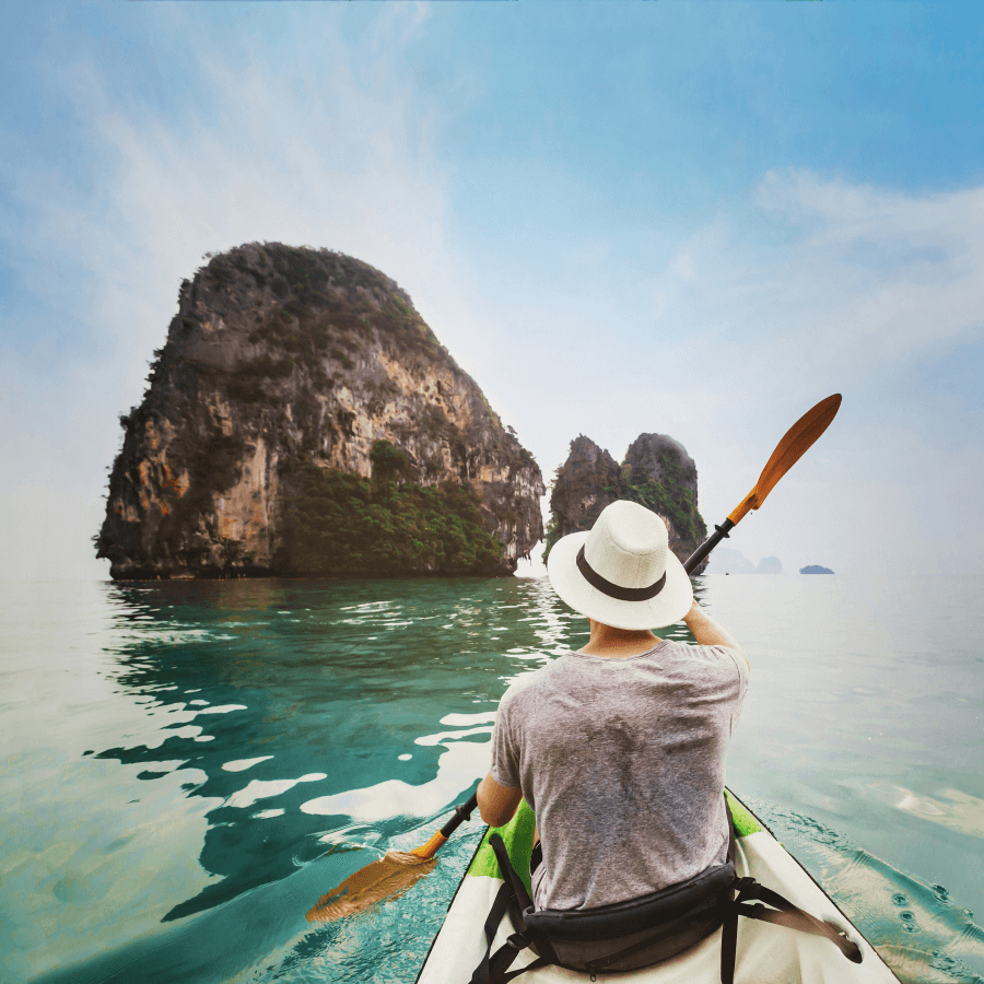 Person kayaking on clear water towards green rocky islands under a clear sky.