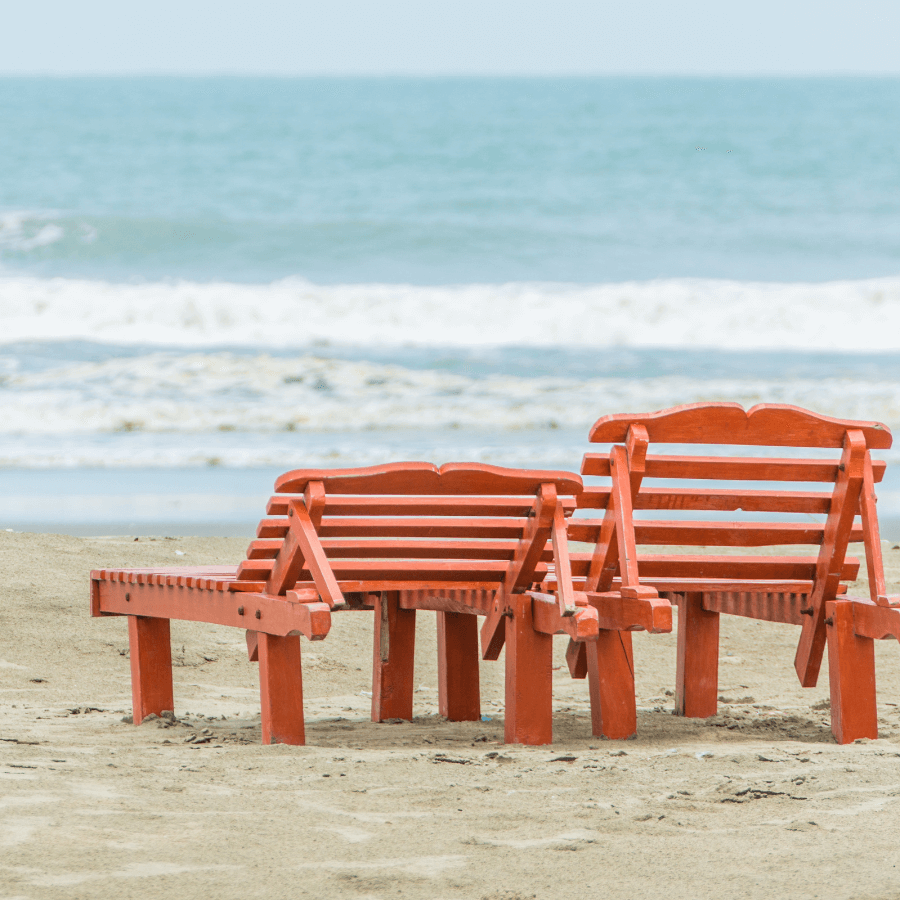 Empty beach with two red benches and overcast skies, illustrating the calmness of off-peak travel.