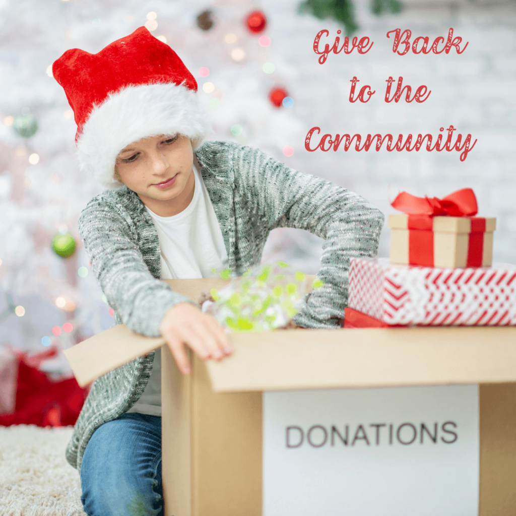 A person wearing a Santa hat and a gray cardigan, placing items into a cardboard box labeled 'DONATIONS' next to a Christmas tree and wrapped gifts. The background is festive with holiday decorations. Text reads, 'Give Back to the Community.