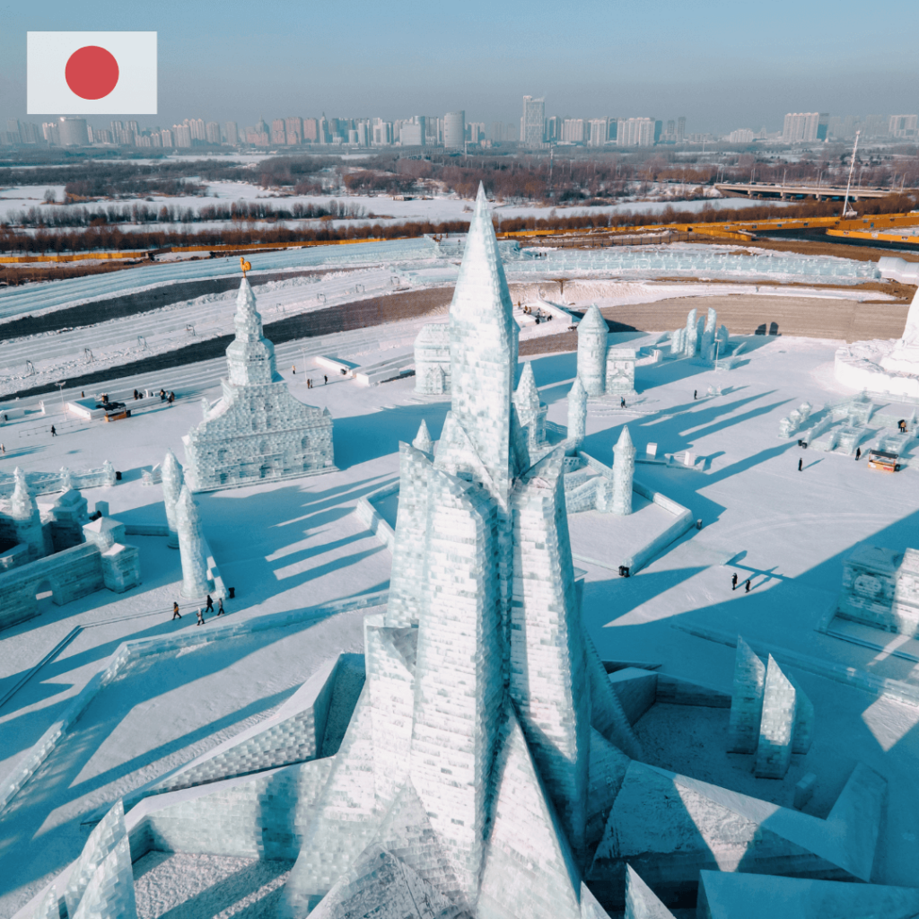 Expansive ice sculpture park in Sapporo, Japan, featuring intricate ice structures resembling castles and towers, with the cityscape in the background and a few people walking around.