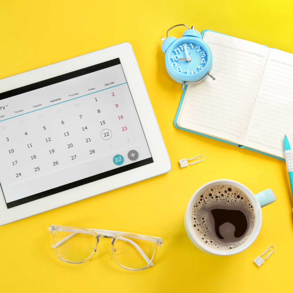 A workspace with a tablet displaying a January calendar, an alarm clock set to 10:10, an open notebook with a pen, eyeglasses, a cup of coffee, and paper clips. Key dates are highlighted. The image emphasizes setting clear daily goals for better time management and productivity.