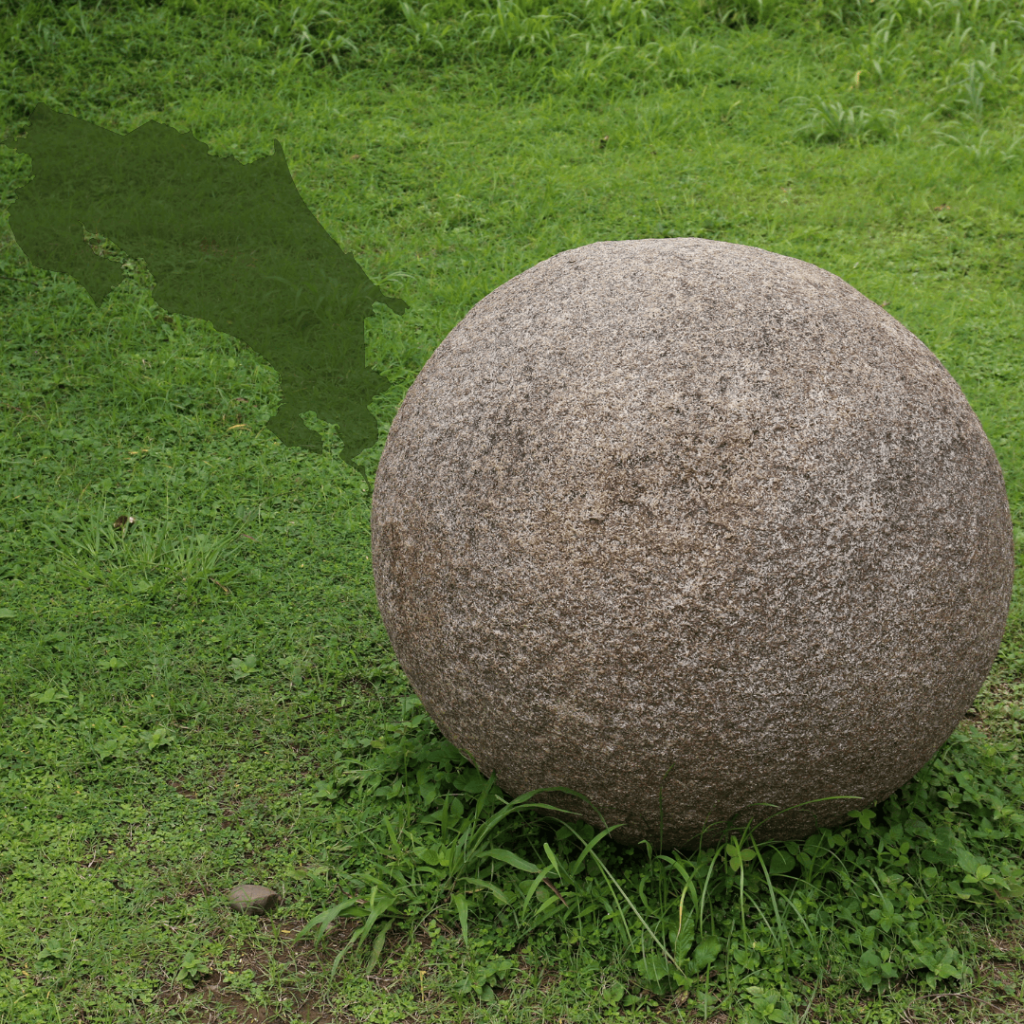 A large, smooth, spherical stone, part of the famous stone spheres of Costa Rica, resting on a grassy area. The background features a faint outline of the map of Costa Rica, highlighting the cultural and historical significance of these pre-Columbian artifacts known for their nearly perfect round shapes.